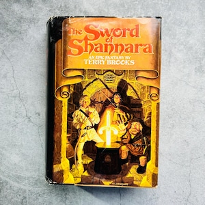 Puede incluir: Un libro de bolsillo vintage titulado "The Sword of Shannara" de Terry Brooks. La portada presenta tres figuras y una espada brillante en un entorno de fantasía, con una combinación de colores naranja y marrón.