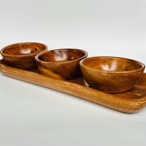 Könnte beinhalten: Ein Set aus drei kleinen Holzschalen mit einem rechteckigen Holztablett. Die Schalen sind braun und haben eine glatte, polierte Oberfläche. Das Tablett ist ebenfalls braun und hat eine etwas rauere Textur.