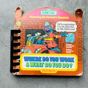 Peut inclure: Livre vintage de Sesame Street intitulé "Where Do You Work & What Do You Do ?" avec Grover le Muppet en pompier. La couverture est orange avec un fond de briques et le texte "Sesame Street" et "Playskool".