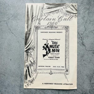 以下が含まれることがあります： 1960年の「The Music Man」ミュージカルのヴィンテージシアタープログラム。白黒のデザインで、タイトル、キャスト、オルフェウム劇場での公演日が含まれています。デザインにはカーテンとフレームが含まれています。