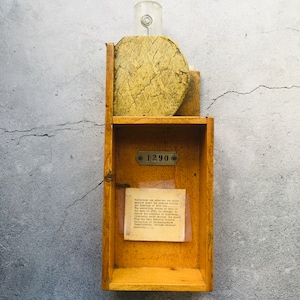 Puede incluir: Una caja de madera con un frasco de vidrio en la parte superior y un pequeño letrero que dice "1290". La caja tiene un pequeño trozo de papel en el interior con texto sobre la historia y los orígenes de la caja.