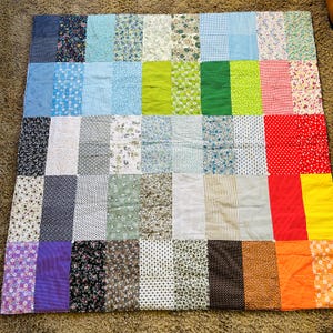 May include: A patchwork quilt with a variety of fabrics in a grid pattern. The quilt features squares of floral, polka dot, striped, and solid fabrics in shades of blue, green, red, orange, and purple.