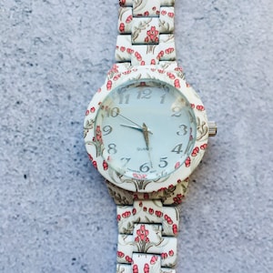 Peut inclure: Montre-bracelet blanche avec un bracelet à motif floral et un cadran blanc avec des chiffres et des aiguilles noirs. Le cadran de la montre indique également "QUARTZ" et "SINGAPORE MOV'T".