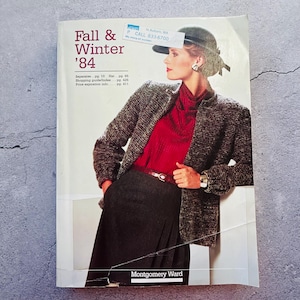 Puede incluir: Un catálogo de Otoño & Invierno '84 de Montgomery Ward con una mujer que lleva una chaqueta de tweed gris, un jersey rojo de cuello alto, una falda negra y un sombrero negro. La portada del catálogo también incluye el número de teléfono 833-6700.