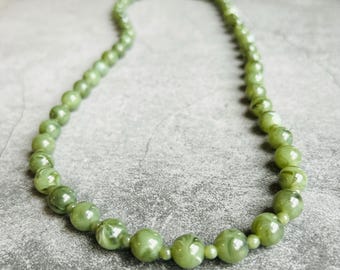 Puede incluir: Un collar de cuentas verdes con efecto marmolado. El collar presenta cuentas redondas de diferentes tamaños, ensartadas para formar un círculo completo. Las cuentas son de color verde claro con veteado blanco.