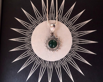 May include: A silver pendant necklace with a green gemstone set in a circular design. The pendant is surrounded by a decorative border of small silver beads. 925 SILVER.