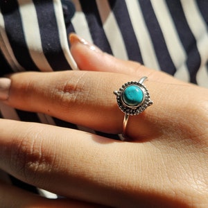 Può includere: Un anello d'argento con una pietra turchese incastonata in una montatura decorativa. L'anello è su un dito.