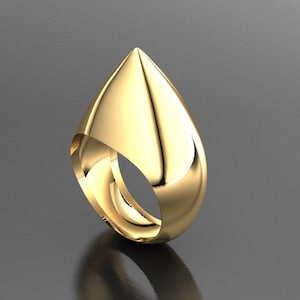 May include: A gold-colored ring with a teardrop-shaped design. The ring has a smooth, polished surface and a pointed top. The band curves around to form the ring's base, creating an open design. The ring is displayed on a reflective surface.