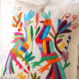 May include: A white pillow with colorful embroidered birds and flowers. The birds are multi-colored with long, flowing tails. The flowers are purple and pink.