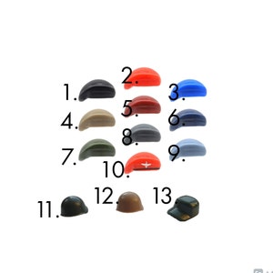 May include: A selection of miniature hats in a range of colours, such as black, red, blue, beige, grey, and green. Some are berets, others are baseball caps or military-style hats. The hats are displayed against a white backdrop.