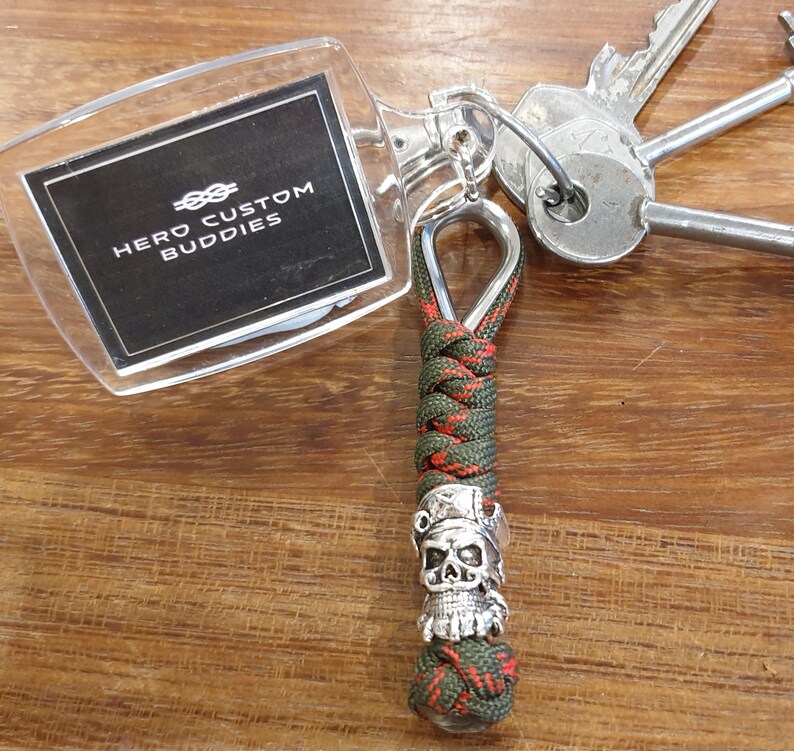May include: Green and red paracord keychain with a silver skull bead and a clear plastic tag that says "HERO CUSTOM BUDDIES".