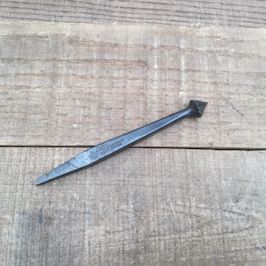 May include: A dark gray metal tool with a pointed tip and a triangular head. The shaft features stamped text that reads "WEATHERVANE BEST STEEL". The tool has a tapered, elongated body with a smooth, matte finish and a distinct, sharp-edged design.