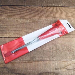 May include: A red and silver dental tool in a clear plastic package with red and white accents. The package has a black hanging hole. The tool is labeled "FOOTPRINT". The package is on a wooden surface.