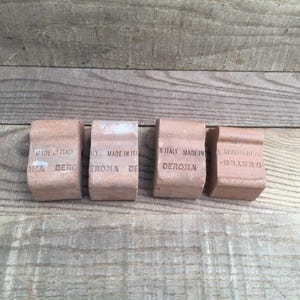 May include: Four terracotta clay pot feet, each featuring a curved design. The text "MADE IN ITALY" and "DEROMA" is stamped on the front of each piece. These small, rectangular supports are designed to elevate containers off the ground.