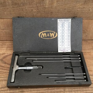 May include: A white ceramic mug with a black handle and the text "But First, Coffee" in a black, handwritten-style font. The mug is on a white surface.