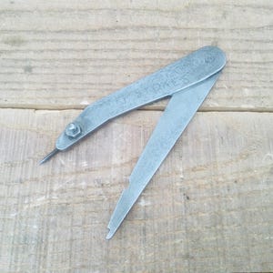 May include: A silver metal tool with a pointed tip and a graduated scale. The tool is labelled "T.S. & CO."