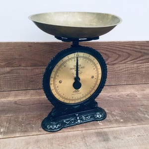 May include: An antique James Family Scale with a brass bowl and a black cast iron base. The scale features a circular dial with black numbers and markings on a gold background. The scale is designed to measure weight.