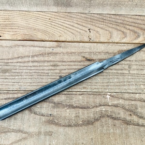 May include: A dark gray metal woodturning gouge featuring a long, curved, semi-circular blade that tapers to a sharp, pointed tip. The tool has a smooth, metallic finish with visible dark oxidation and a stamped brand mark near the neck.