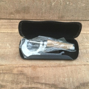 May include: A silver micrometer tool in a black case. The tool is partially visible, with a curved measuring end and a cylindrical handle. The case is open, revealing the tool inside. The background is a wooden surface.