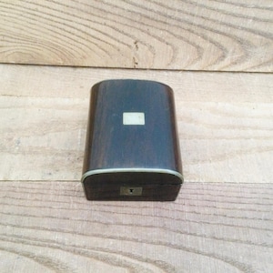 May include: A dark brown wooden box with a rectangular shape and a small, light-coloured square on the top. The box has a metal trim and a keyhole on the front. The box is on a wooden surface.