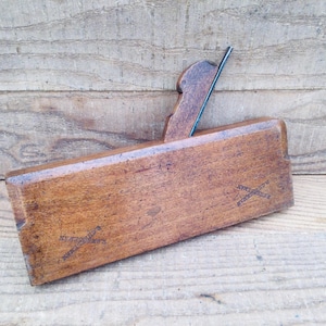 May include: A vintage wooden hand plane with a dark brown finish. The plane has a blade and a handle. The wood grain is visible. The plane is resting on a wooden surface. The text "E.C. STEARMAN" is stamped on the side.
