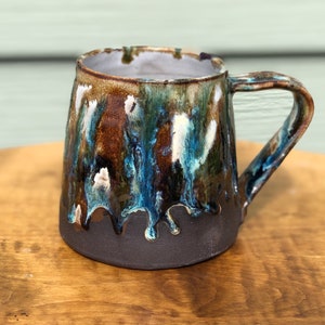 May include: A ceramic mug with a brown, blue, and white glaze. The glaze has a drip effect, giving the mug a unique and rustic look.
