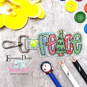 May include: Embroidered Christmas-themed keychain with the word "Peace" in colorful letters and a green Christmas tree in the center. The keychain is attached to a silver metal key ring.