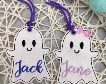 May include: Two white ghost-shaped ornaments with purple and pink glitter. The ghost on the left has the name "Jack" embroidered in blue thread. The ghost on the right has the name "Jane" embroidered in pink thread and a pink bow.