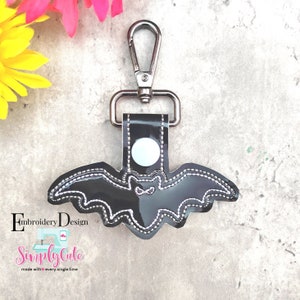 May include: Black bat-shaped keychain with a silver swivel clip. The bat has a white outline and a small white eye.