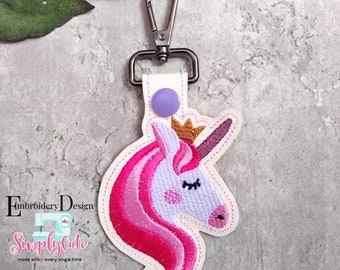 May include: A pink and purple unicorn head keyring with a gold crown and a purple button. The keyring is attached to a silver metal clip.