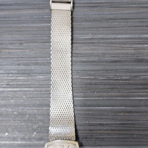 May include: A silver watch with a square face and a silver mesh band. The watch face has Roman numeral hour markers and a white background. The watch is a vintage style.