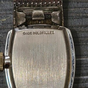 May include: A silver watch with a square face and a metal band. The back of the watch has the words "10K Gold Filled" engraved on it.