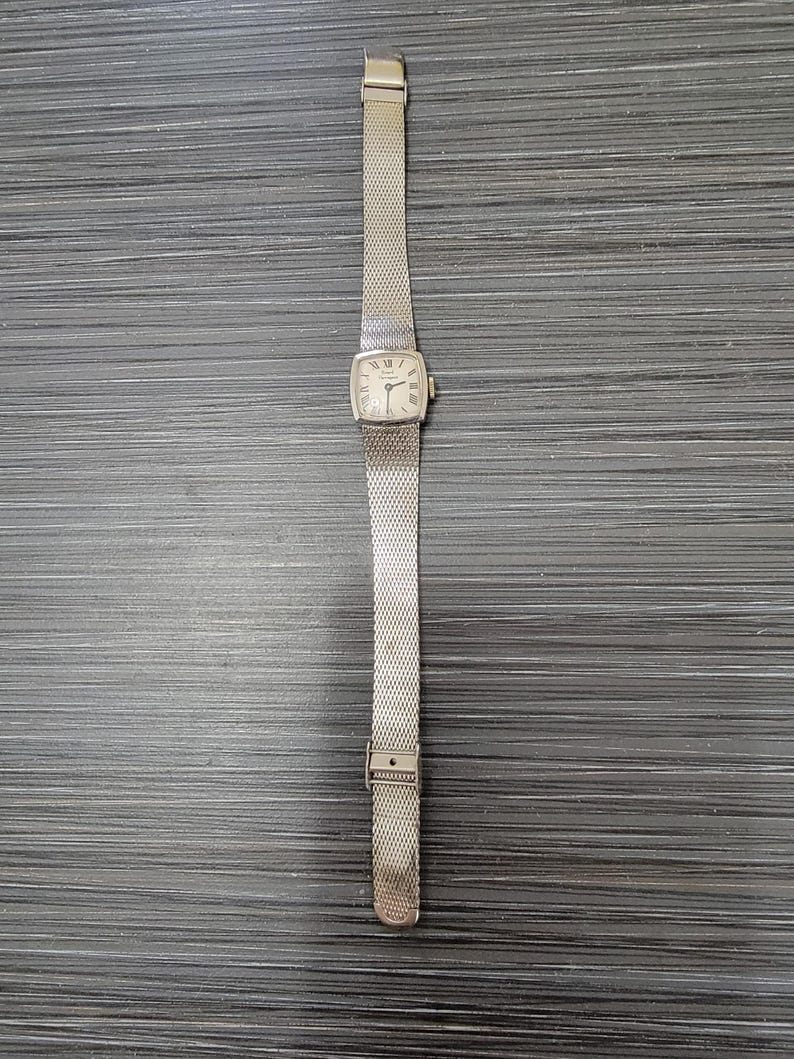 May include: A silver watch with a square face and a silver mesh band.