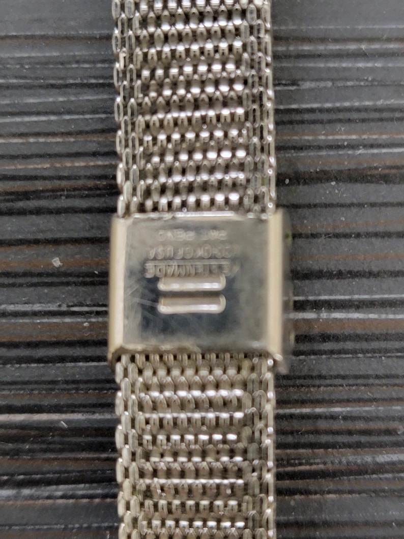 May include: Silver metal watch band with a clasp that reads "GENUINE STAINLESS STEEL CASE NO. 154".