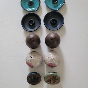 May include: A selection of ceramic salt and pepper shakers and candle holders. The set includes teal and black candle holders, brown and speckled salt and pepper shakers, and decorative leaf and flower-shaped pieces.