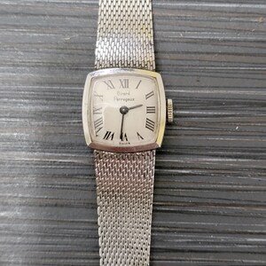 May include: A silver wristwatch with a square face and a silver mesh band. The watch face has Roman numeral hour markers and the text "Girard Perregaux" printed on it.