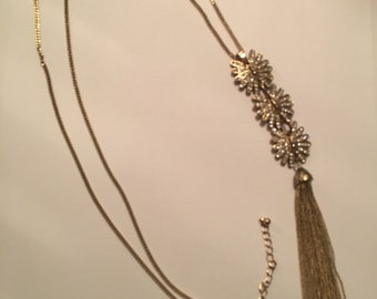 May include: A gold chain necklace with a tassel pendant featuring a cluster of sparkling rhinestones.