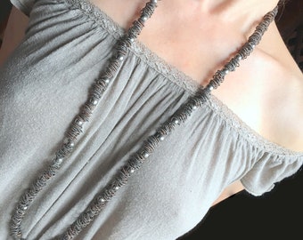 May include: A long silver and copper necklace with small round beads. The necklace is worn by a person with a light gray off-the-shoulder top.