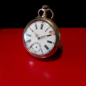 May include: A silver pocket watch with Roman numeral hour markers and a white face. The watch is on a red surface.
