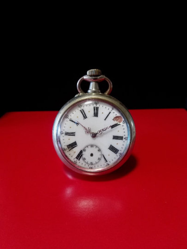 May include: A silver pocket watch with Roman numeral hour markers and a white face. The watch has a small second hand dial at the bottom of the face.