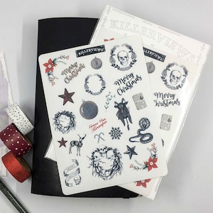 Könnte beinhalten: Aufkleberbögen mit einem düsteren Weihnachtsthema, die Totenköpfe, Kränze und den Text "Merry Christmas" zeigen. Ein schwarzes Notizbuch und dekorative Klebebandrollen sind ebenfalls zu sehen.