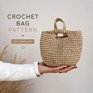 May include: A crocheted bag with a handle, held in a hand. The bag is made of a light brown, woven material. The text "CROCHET BAG PATTERN" is displayed above the bag, with "PDF DOWNLOAD" below.