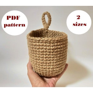 Op de afbeelding: Een gehäkelde jute hangmand met een lusvormig handvat. De mand is beige en heeft een natuurlijke, rustieke uitstraling. De afbeelding bevat de tekst "PDF pattern" en "2 sizes".