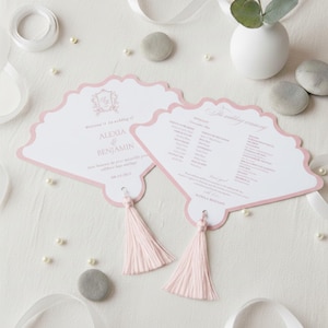 May include: Two fan-shaped wedding programmes with white cardstock and dusty pink borders. Each features a light pink tassel at the base. The text reads Welcome to the wedding of ALEXIA & BENJAMIN 09.20.2025 and The wedding ceremony with listed names.