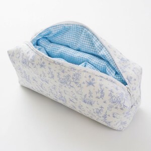 May include: A rectangular cosmetic bag with a white background and a blue toile pattern. The interior is lined with a light blue gingham fabric. The bag is open, revealing the interior.