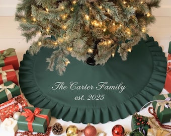 May include: A dark green Christmas tree skirt with a ruffled edge, personalized with "The Carter Family est. 2025" in white script. The skirt is under a decorated Christmas tree with red ornaments and fairy lights. Presents surround the tree.