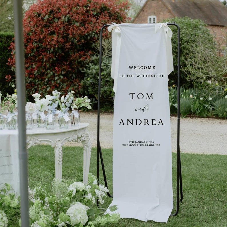 Op de afbeelding: Witte bruiloft welkom bord met zwarte tekst die "Welkom op de bruiloft van Tom en Andrea, 8 januari 2023, The McCallum Residence" luidt.
