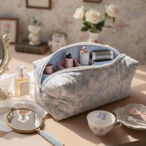 May include: A quilted cosmetic bag with a blue floral pattern and a gingham lining. The bag is open, revealing various beauty products. A perfume bottle, a hand mirror, and a teacup are also visible.