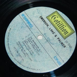 May include: A blue and white vinyl record label with the text "Cotillion SD 9040 Emerson, Lake & Palmer" and the song titles "The Barbarian", "Take A Pebble", and "Knife-Edge".