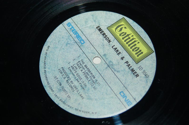 May include: A blue and white vinyl record label with the text "Cotillion SD 9040 Emerson, Lake & Palmer" and the song titles "The Barbarian", "Take A Pebble", and "Knife-Edge".